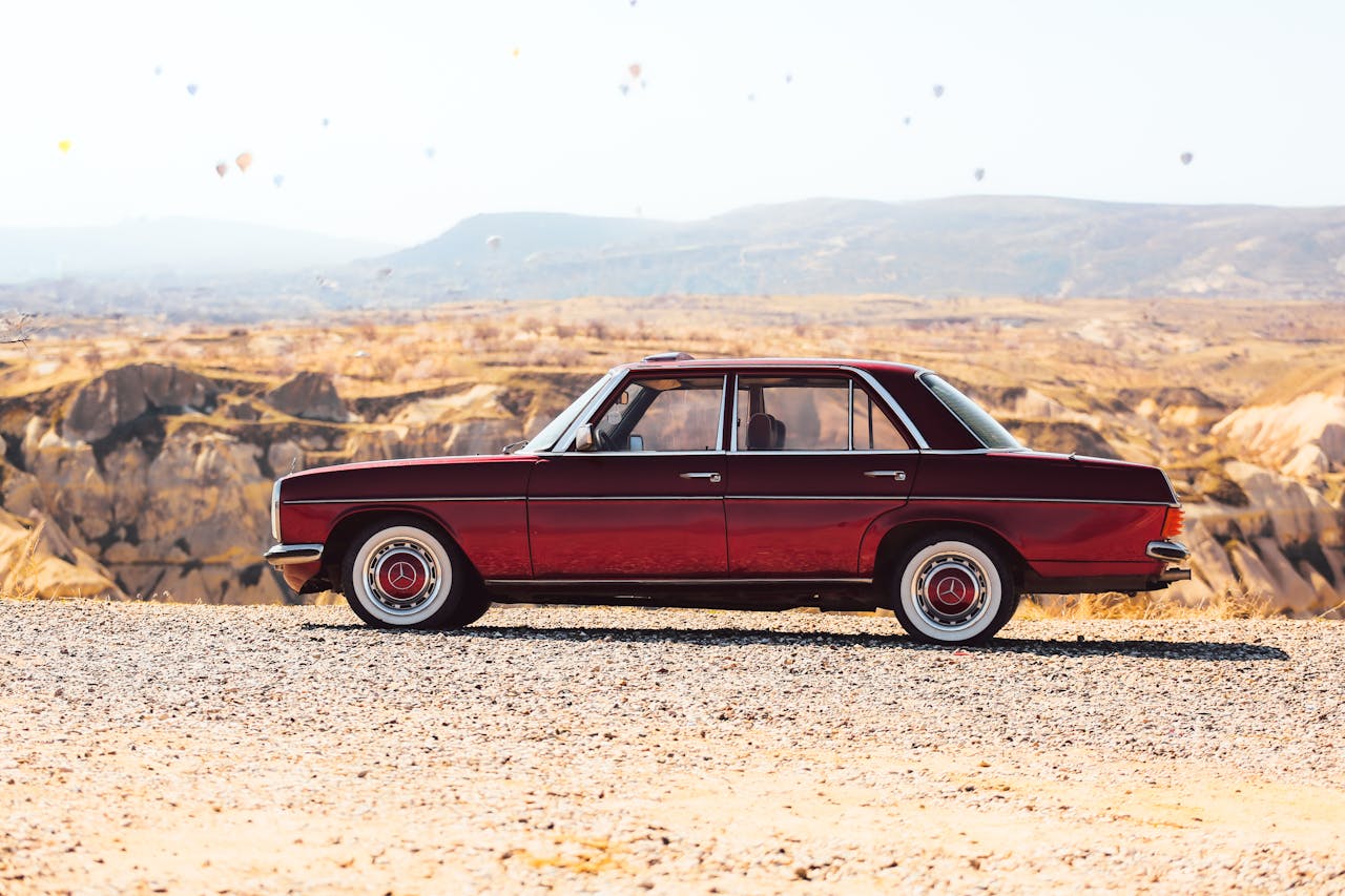 Vintage red Mercedes car with hot air balloons in Cappadocia, Turkey, showcasing stunning landscape.